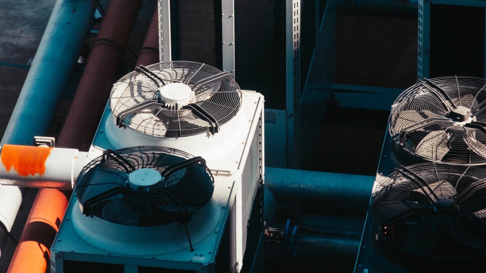 A bank of rooftop air-conditioning condenser units with large fan grilles, connected by insulated refrigerant and service pipework.
